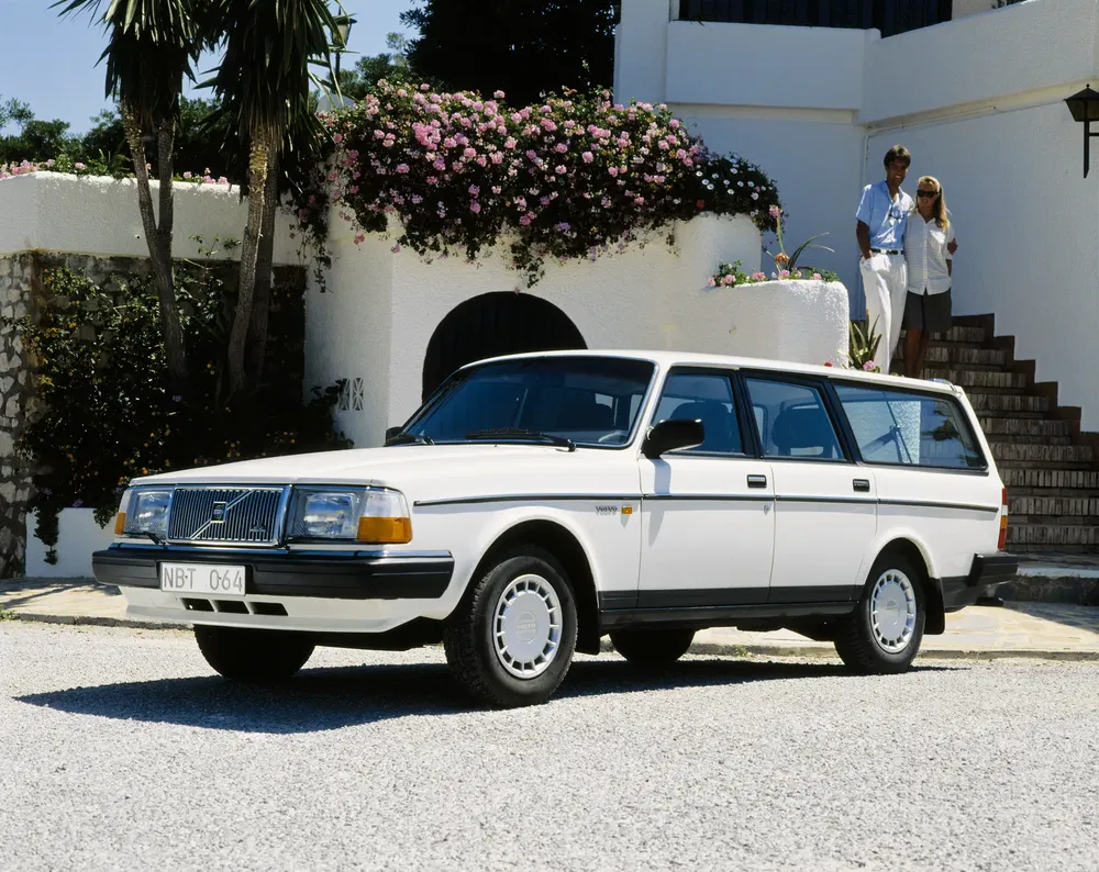 Volvo 245 break blanc garé devant une villa méditerranéenne avec végétation florale.