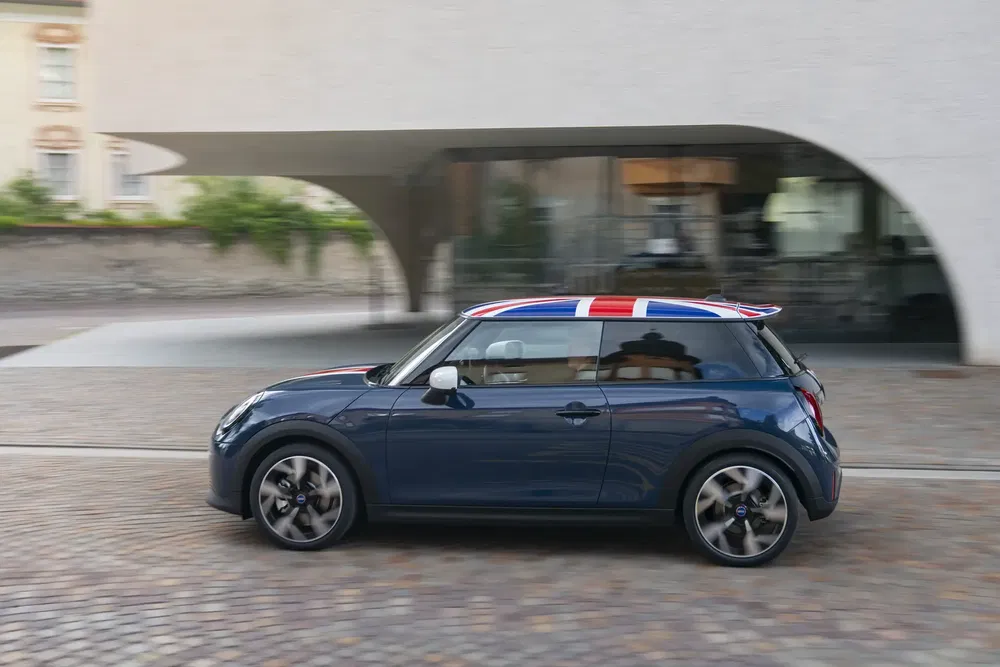 Mini Cooper bleu avec toit drapeau britannique, roulant en ville.