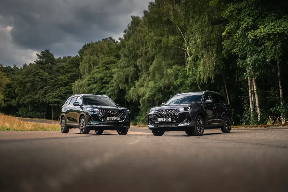 Deux Audi Q5 noires garées sur une route entourée de forêt dense, ciel nuageux.