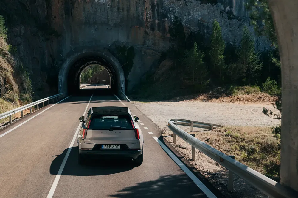 Voiture Volvo EX30 entrant dans un tunnel sur une route de montagne ensoleillée.