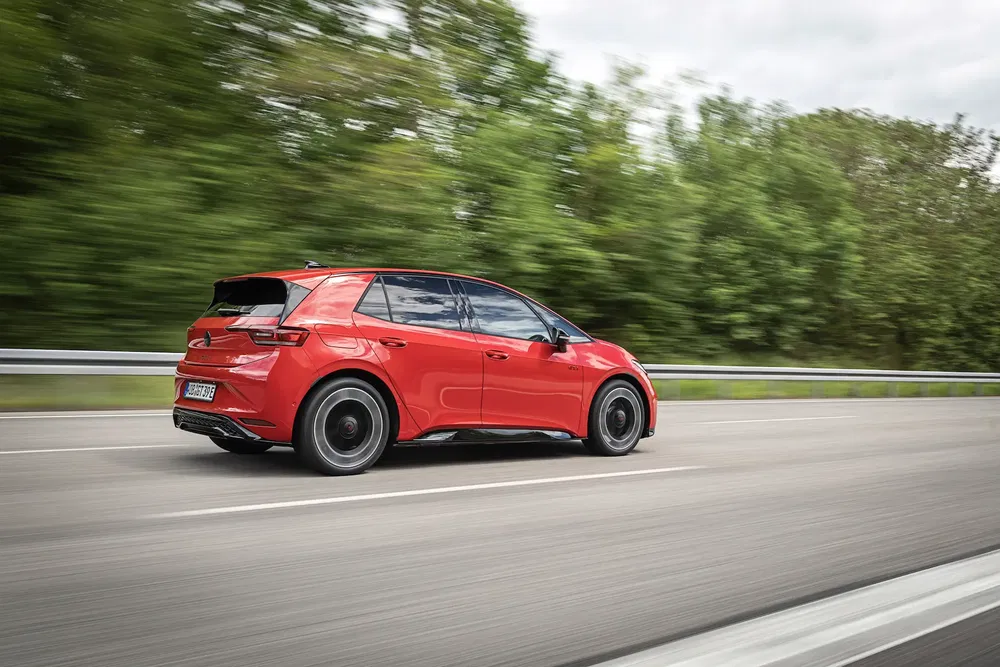 Volkswagen ID.3 rouge roulant rapidement sur une autoroute bordée d'arbres verts.