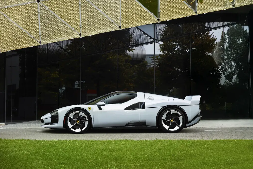 Ferrari concept moderne, gris argenté, devant bâtiment vitré, pelouse verte au premier plan.
