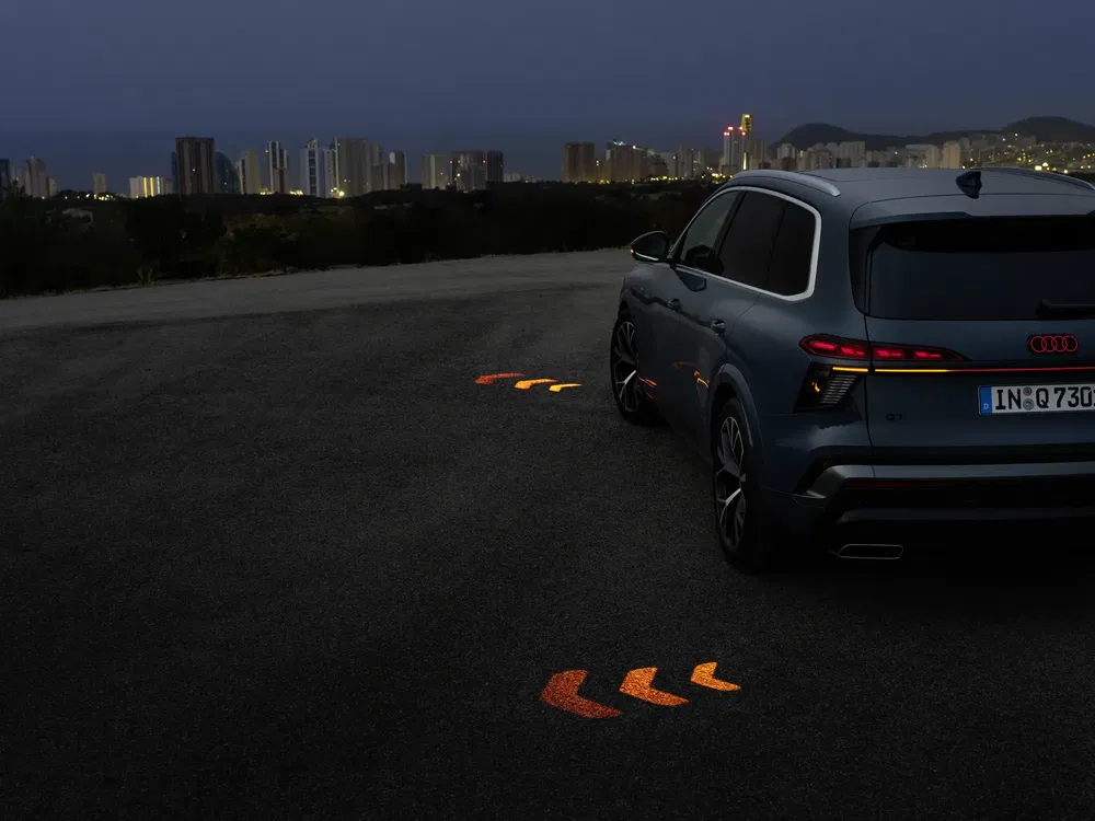 Audi Q3 garé, lumières LED projetées au sol, ville illuminée en arrière-plan.