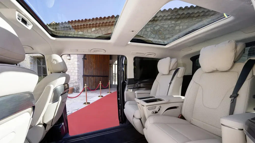 Ruime binnenkant van een luxueuze minivan met panoramisch dak en witte lederen stoelen.