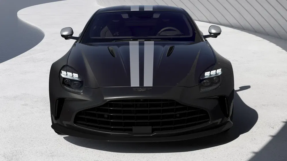 Aston Martin DBS noire avec bandes argentées sur capot, stationnée dans un environnement moderne.