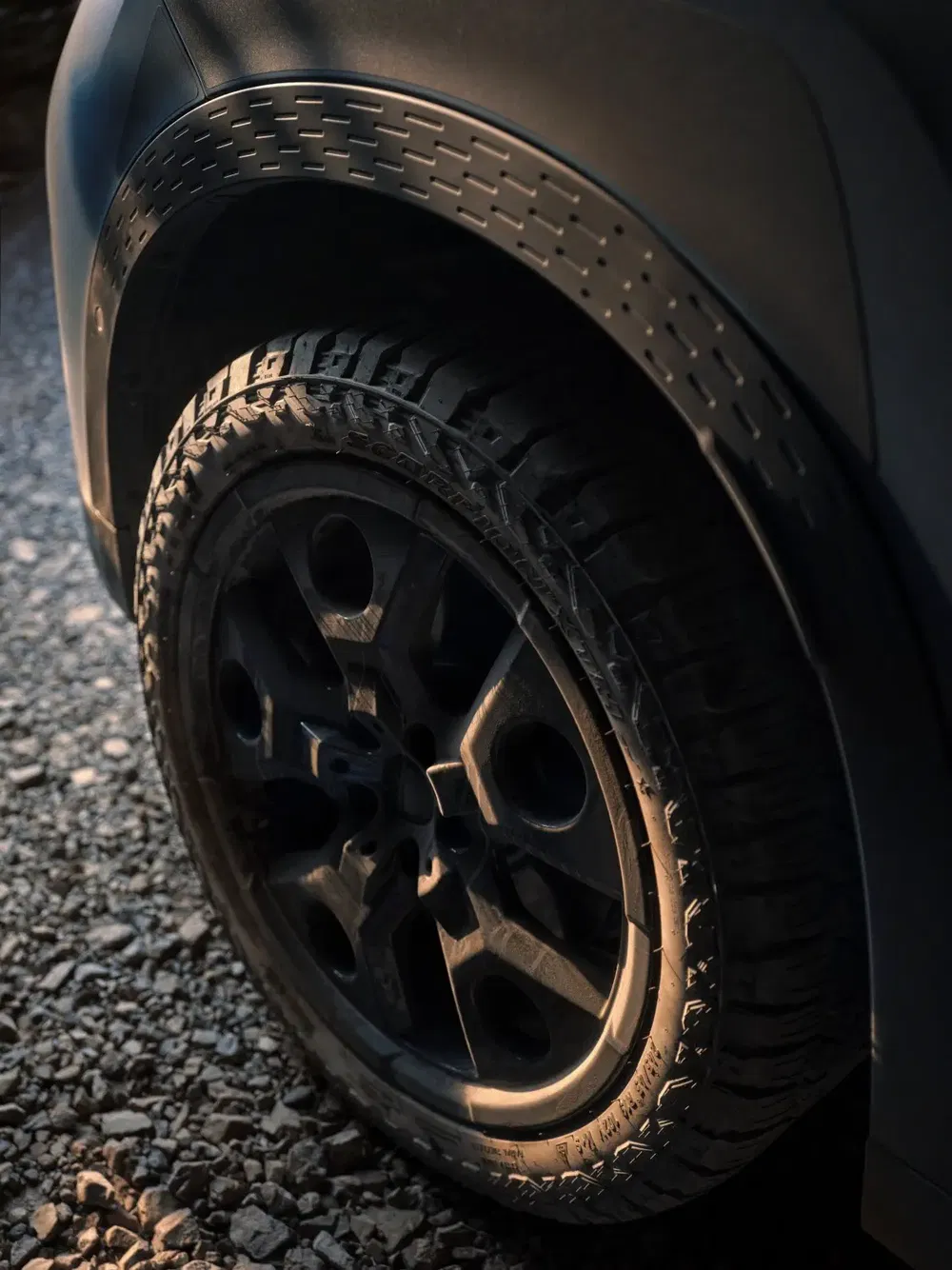 Gros plan sur la roue d'un SUV sur un chemin de gravier au crépuscule.