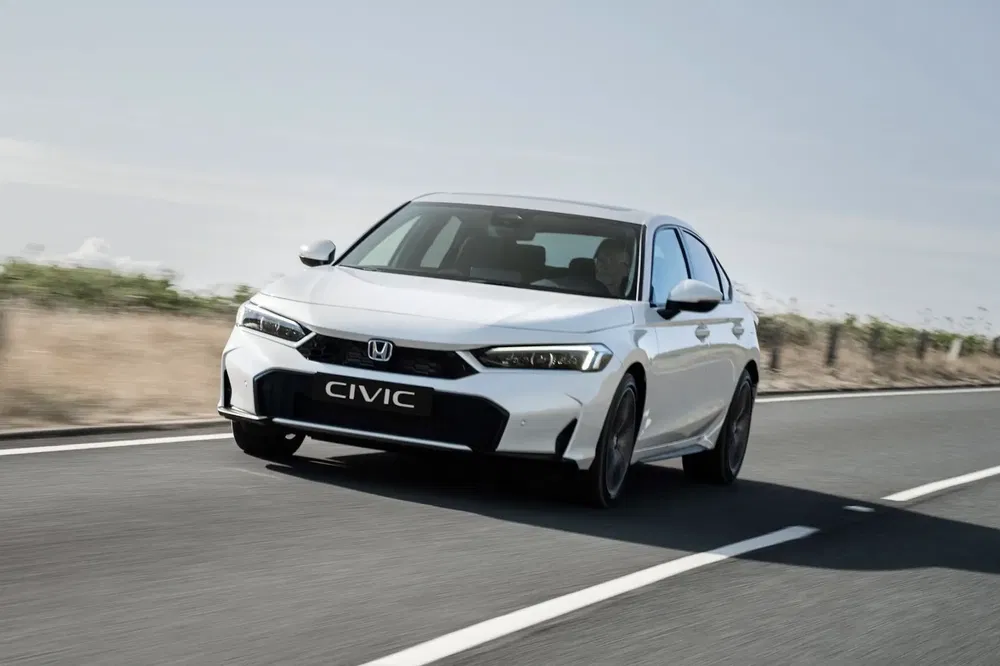 Honda Civic blanche moderne roulant sur une route dégagée en campagne.