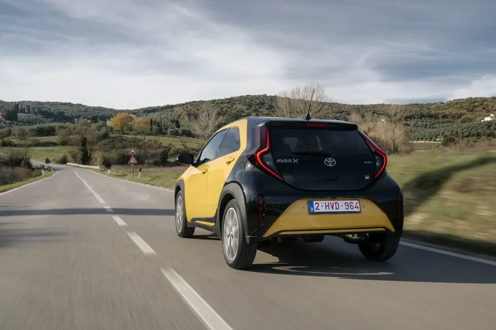 Toyota Aygo X jaune et noir roulant sur une route de campagne dégagée.