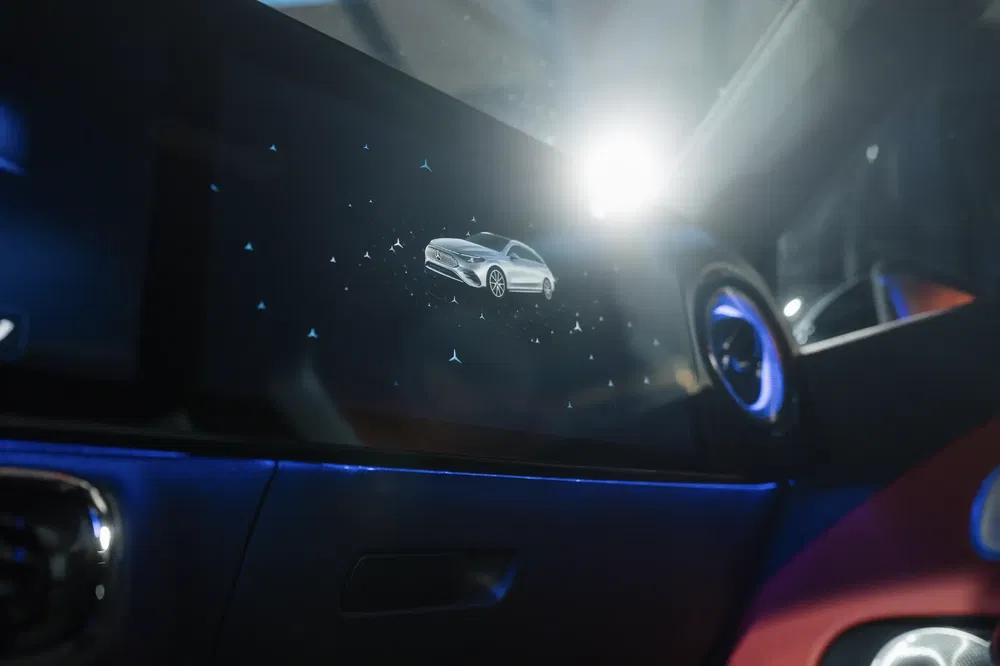 Écran numérique intérieur d'une Mercedes-Benz avec image de voiture argentée moderne, éclairage ambiant bleu.