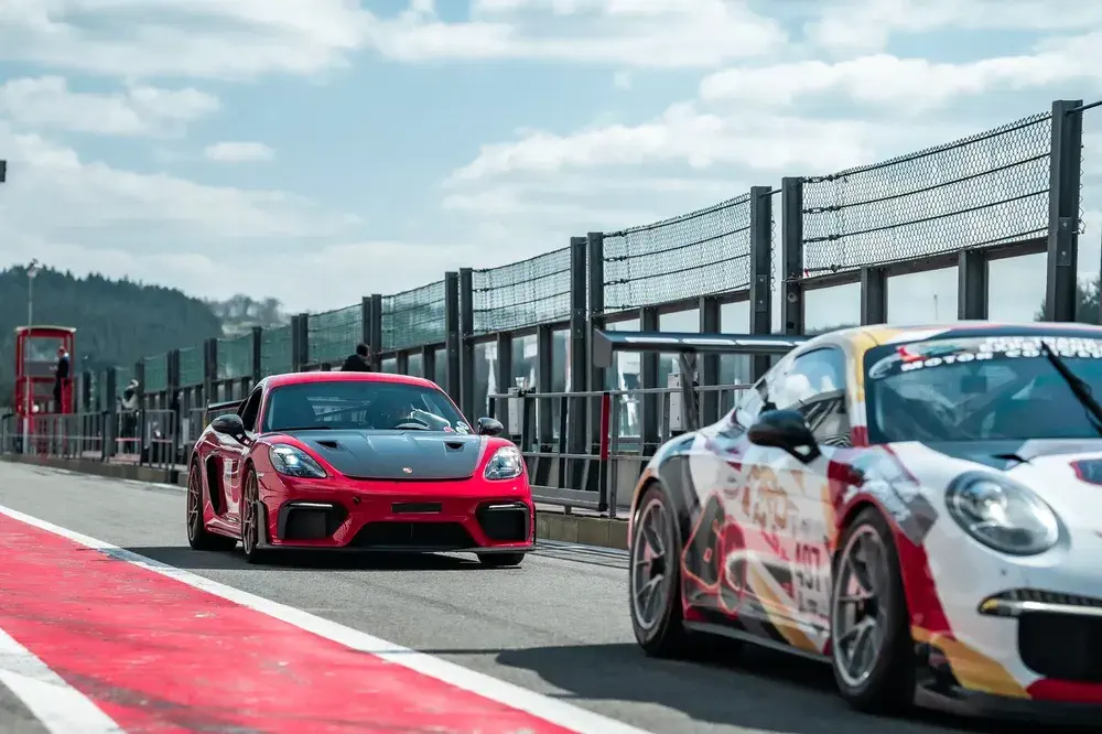 Deux voitures de course Porsche sur la piste, une rouge et l'autre avec livrée multicolore.