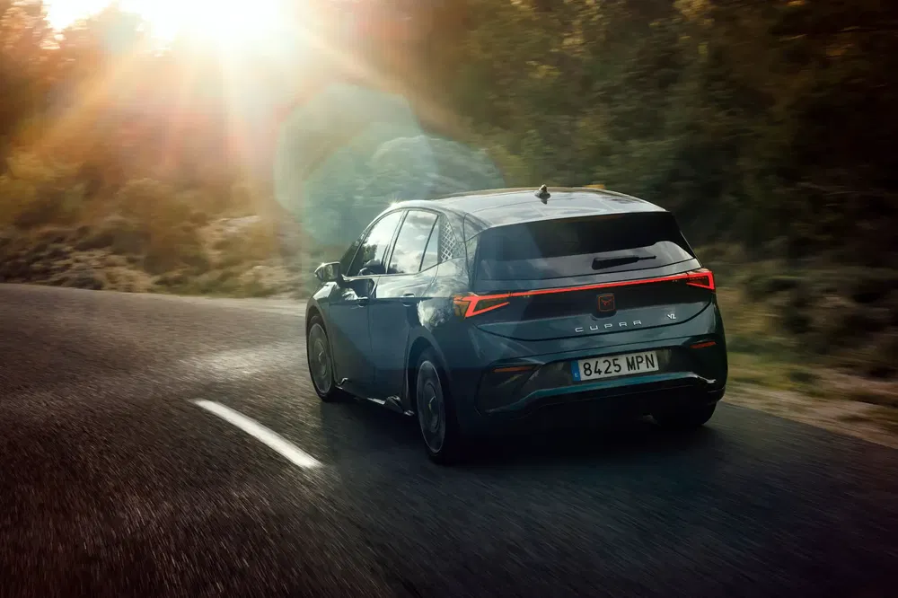 Cupra-auto op kronkelige weg bij zonsondergang, stralend gouden licht erachter.