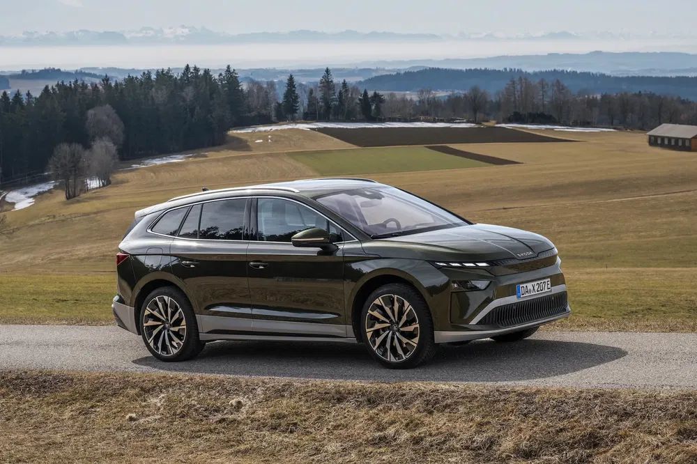 Škoda Enyaq vert roulant sur route panoramique ; collines et forêt en arrière-plan.