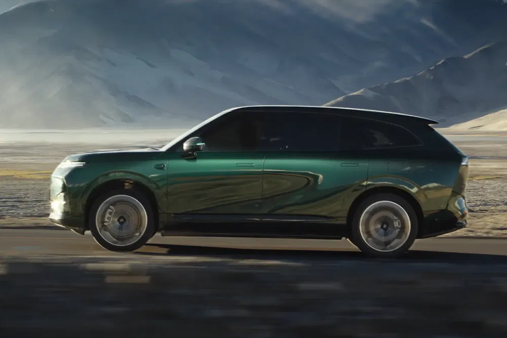 SUV électrique vert foncé roulant sur une route de campagne au pied des montagnes.