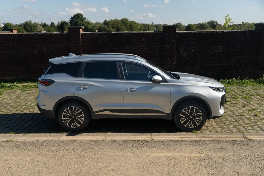 Crossover SUV gris argenté stationné devant un mur de briques par une journée ensoleillée.