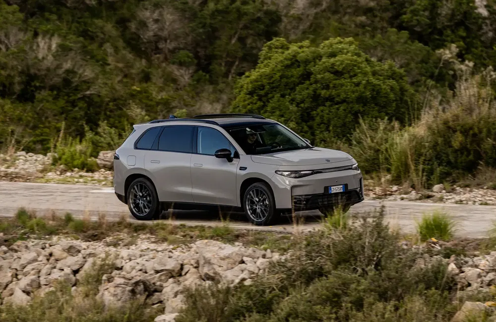 Elektrische HiPhi X SUV rijdt op landweg omringd door groen en rotsen.