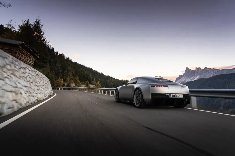 Voiture sportive gris foncé sur route de montagne sinueuse, au crépuscule, panorama alpin.