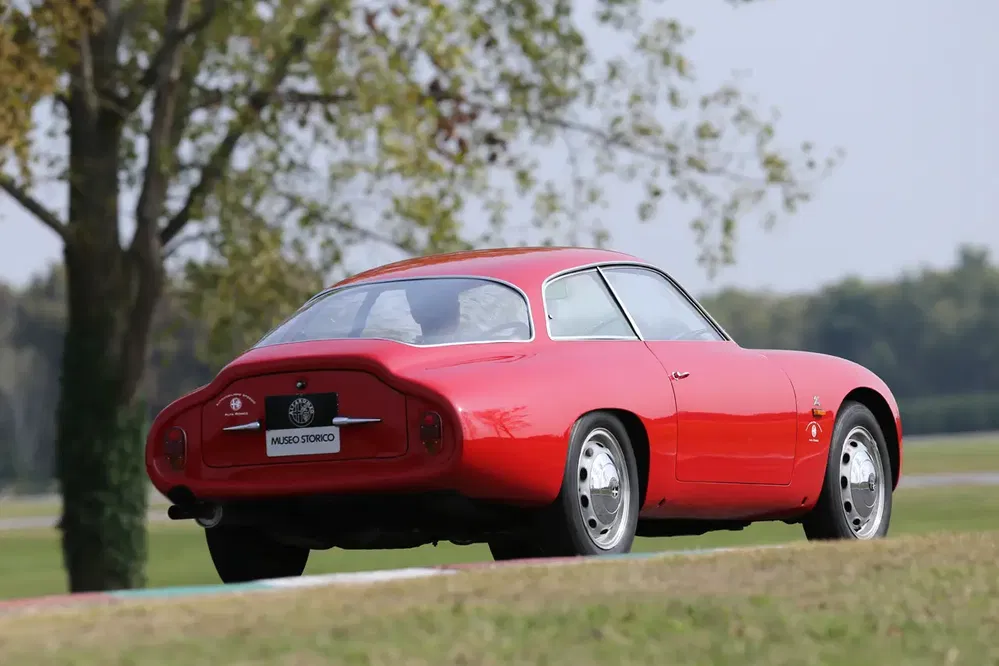 Alfa Romeo Giulietta SZ rouge vintage sur circuit, arrière-plan nature verdoyante.