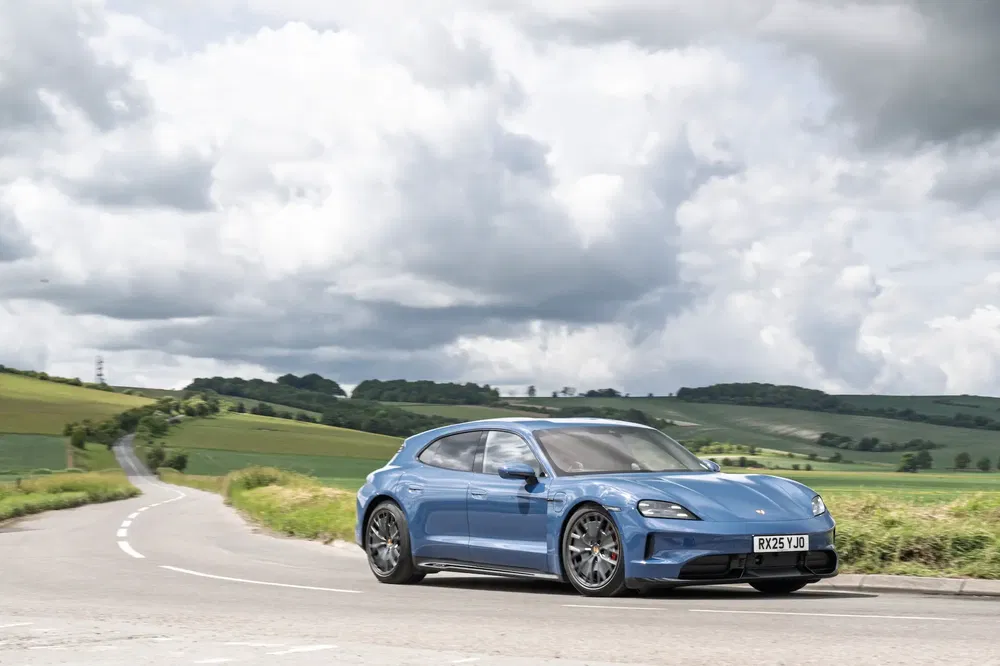 Porsche Taycan Cross Turismo bleu sur route de campagne sous ciel nuageux.