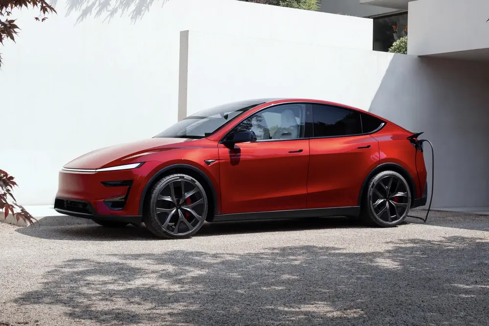 Rode Tesla Model Y elektrische auto wordt opgeladen in een moderne oprit.