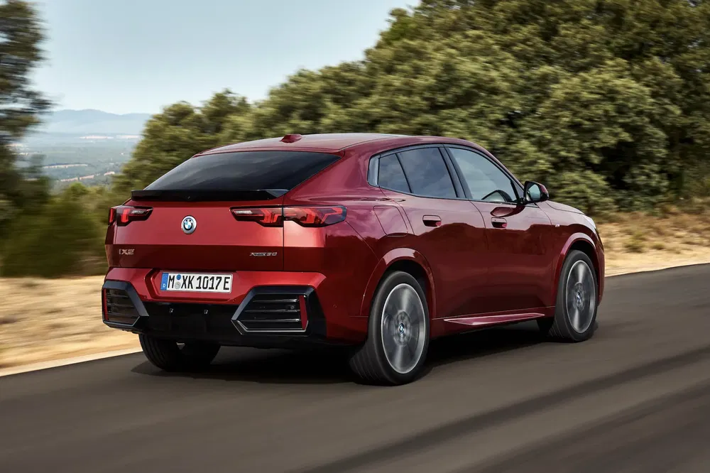 Rode BMW iX2 elektrisch achteraanzicht, rijden op een weg omgeven door groen landschap.