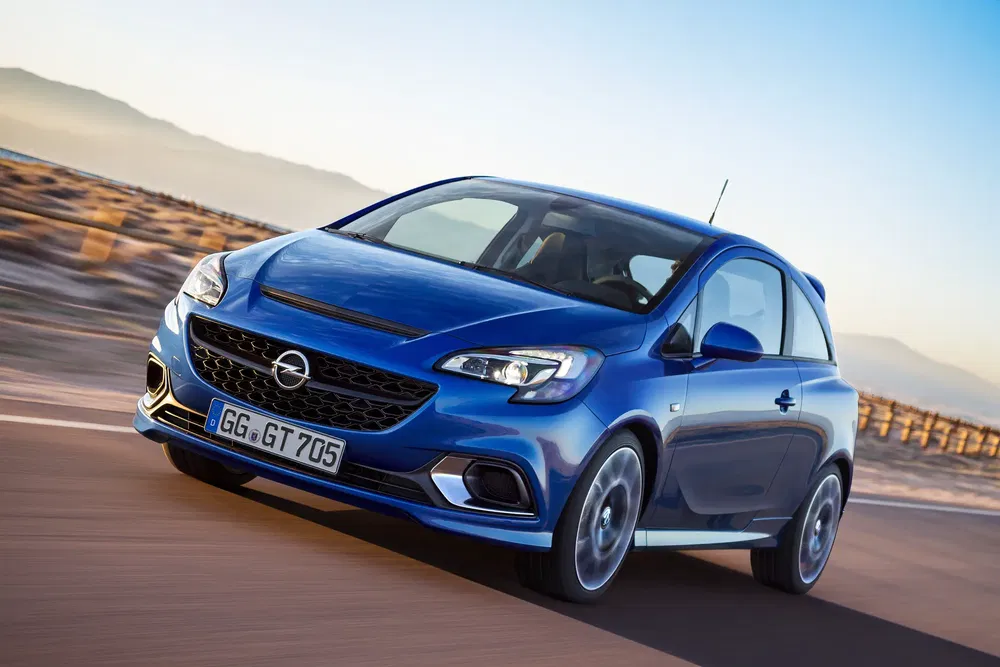 Opel Corsa bleue en mouvement sur une route panoramique au coucher du soleil.