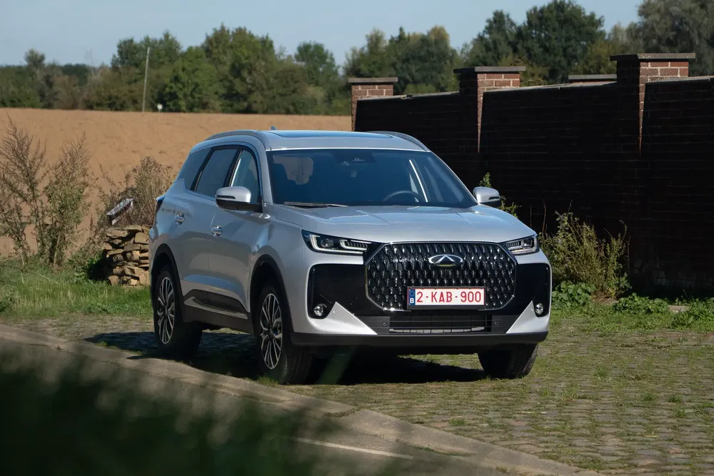 SUV Chery Tiggo 8 argenté garé dans une allée pavée, arrière-plan rural et murs de briques.