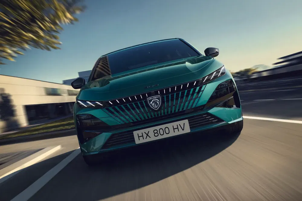 Peugeot 308 vert sur route en mouvement à haute vitesse avec architecture moderne en arrière-plan.