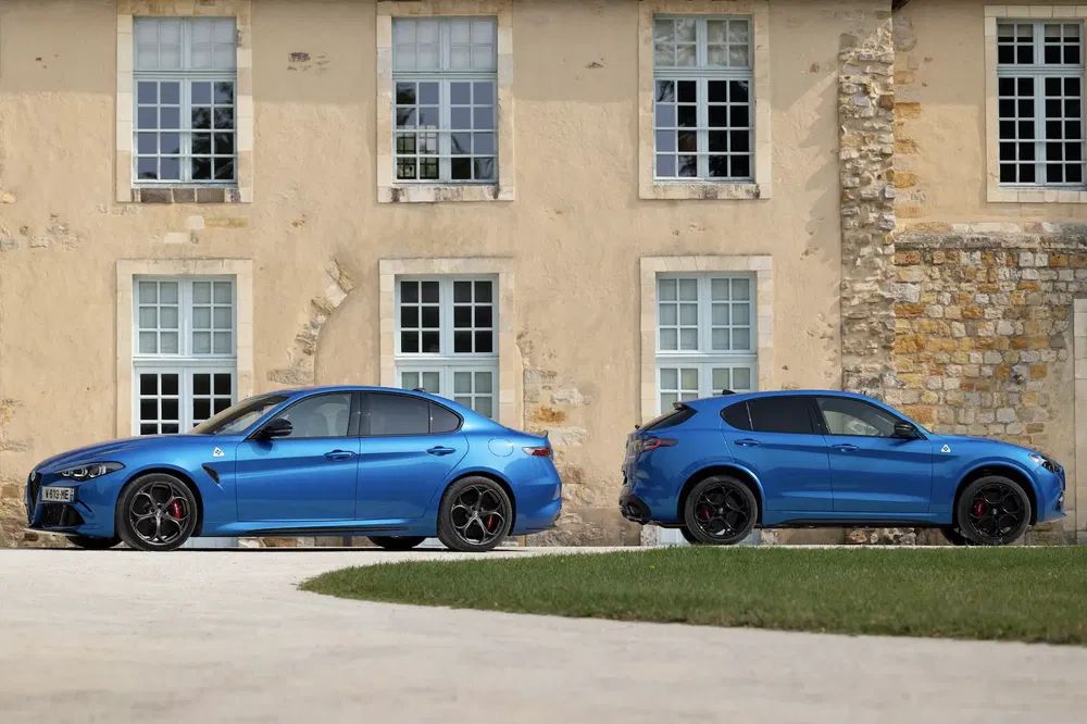 Twee blauwe Alfa Romeo's voor een stenen huis, Giulia en Stelvio Quadrifoglio.