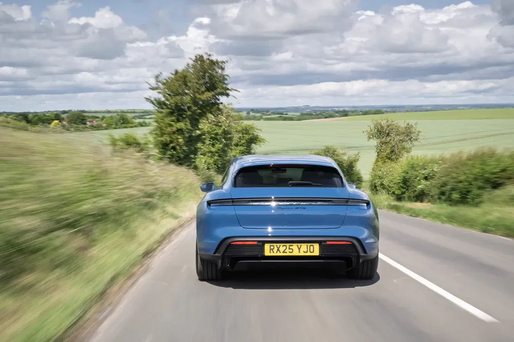 Porsche Taycan bleu roulant sur une route de campagne sous un ciel nuageux.