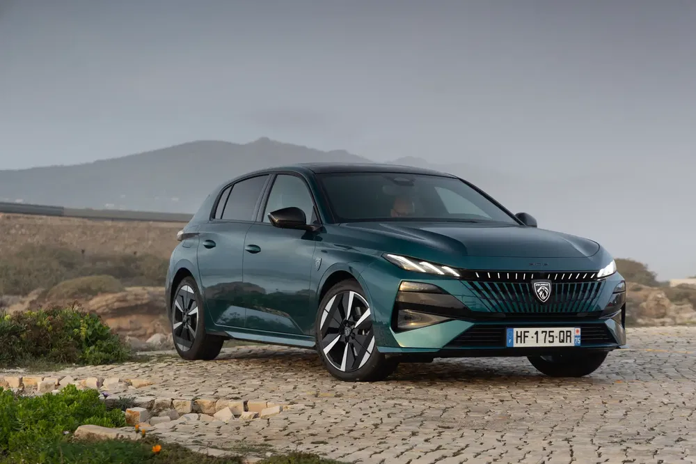 Peugeot 308 2023 op plattelandsweg met bergachtig landschap, stijlvol en modern ontwerp.