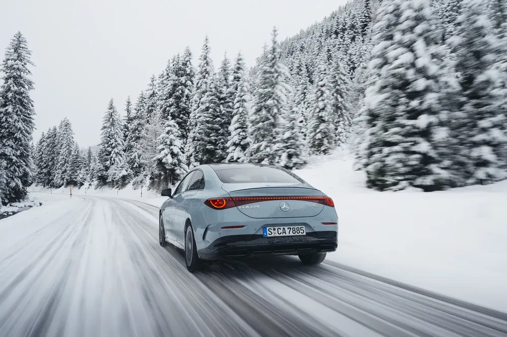 Mercedes-Benz EQE rijdend op een besneeuwde weg, omgeven door met sneeuw bedekte dennenbomen.