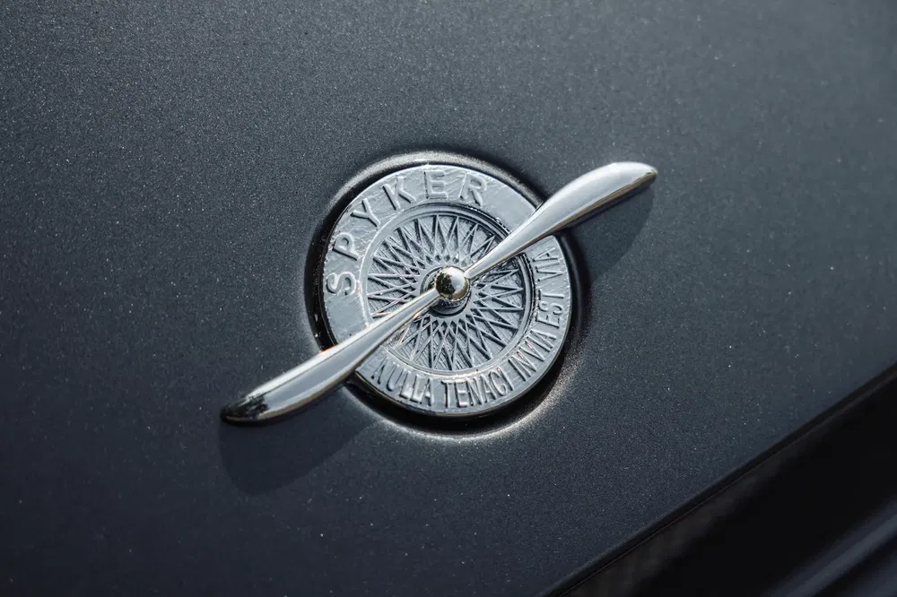 Emblème Spyker en métal sur capot de voiture avec hélice stylisée.
