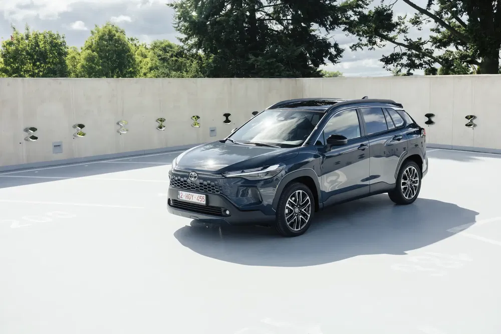Toyota SUV gris sur un parking ensoleillé, entouré de verdure et d'un mur clair.