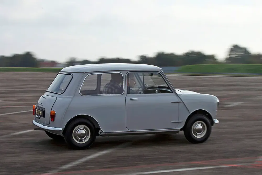 Grijze klassieke Mini rijdend op een baan, iconische auto uit de jaren zestig.