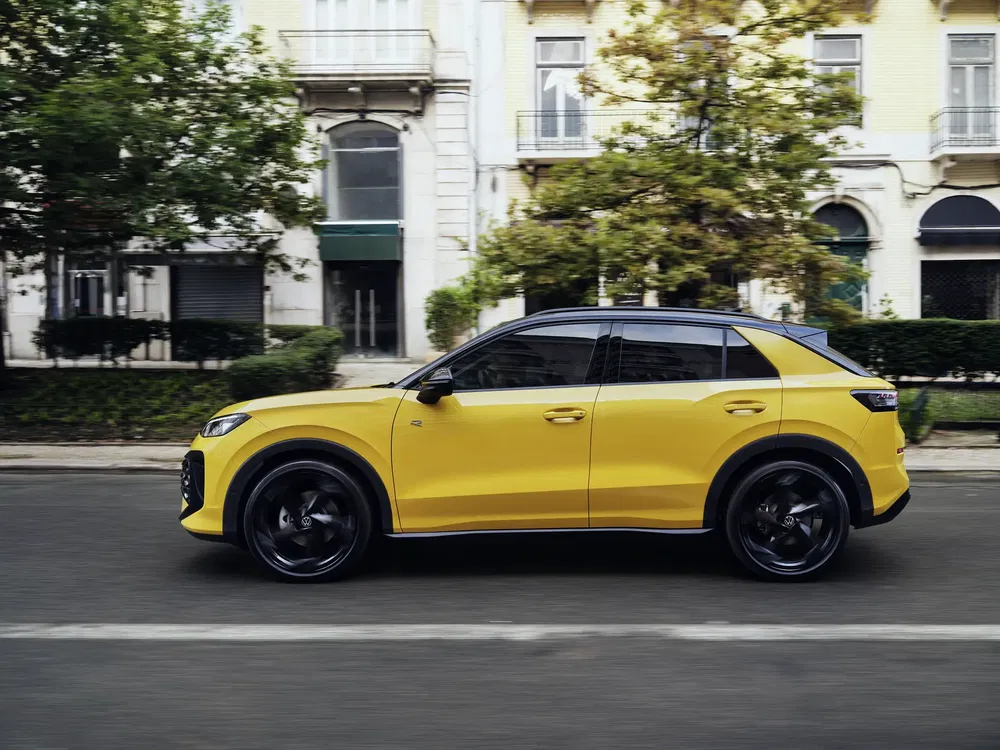 Felgele Volkswagen T-Roc rijdt langs oude gebouwen in een stedelijke omgeving.