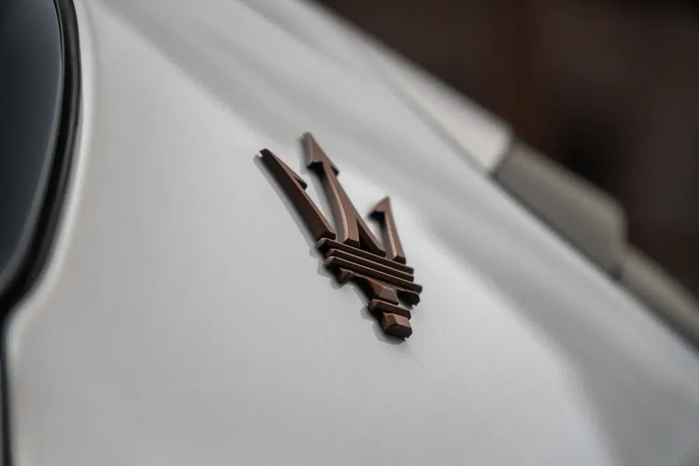 Logo emblématique bronze de Maserati sur carrosserie blanche élégante et lisse.