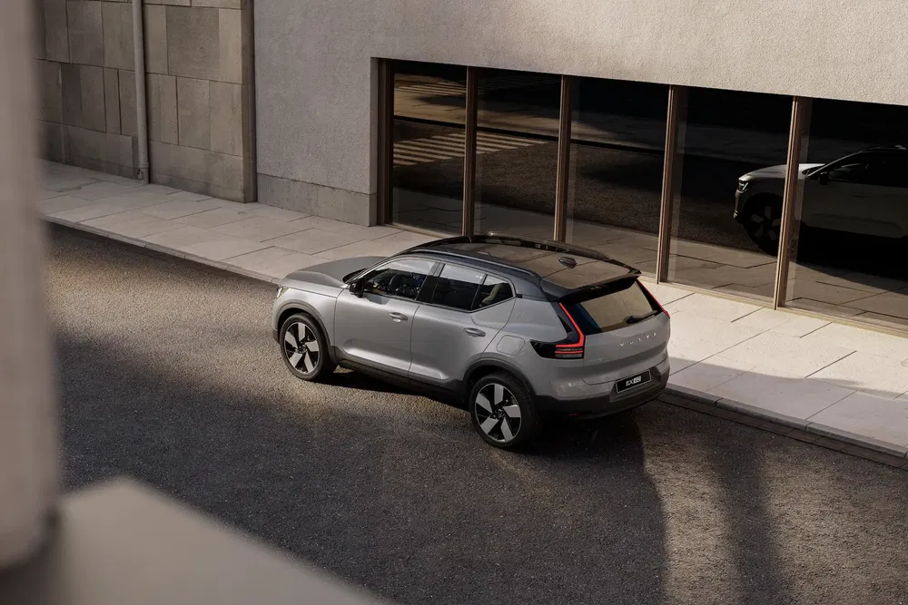 Volvo XC40 gris stationné devant un bâtiment moderne, reflété dans les grandes baies vitrées.