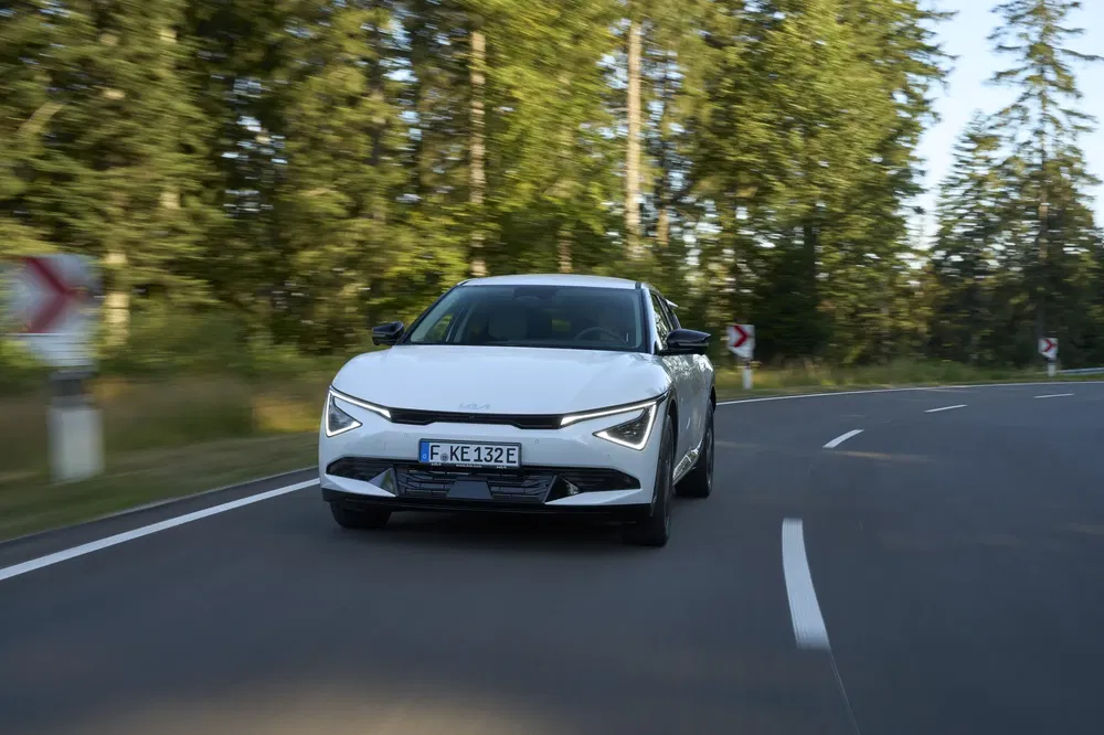 Kia EV6 in het wit rijdt op een bochtige weg omringd door groene bossen.