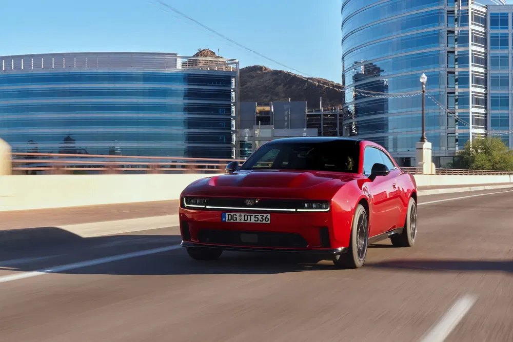 Voiture Dodge Charger rouge moderne roulant sur une autoroute urbaine avec des bâtiments en arrière-plan.