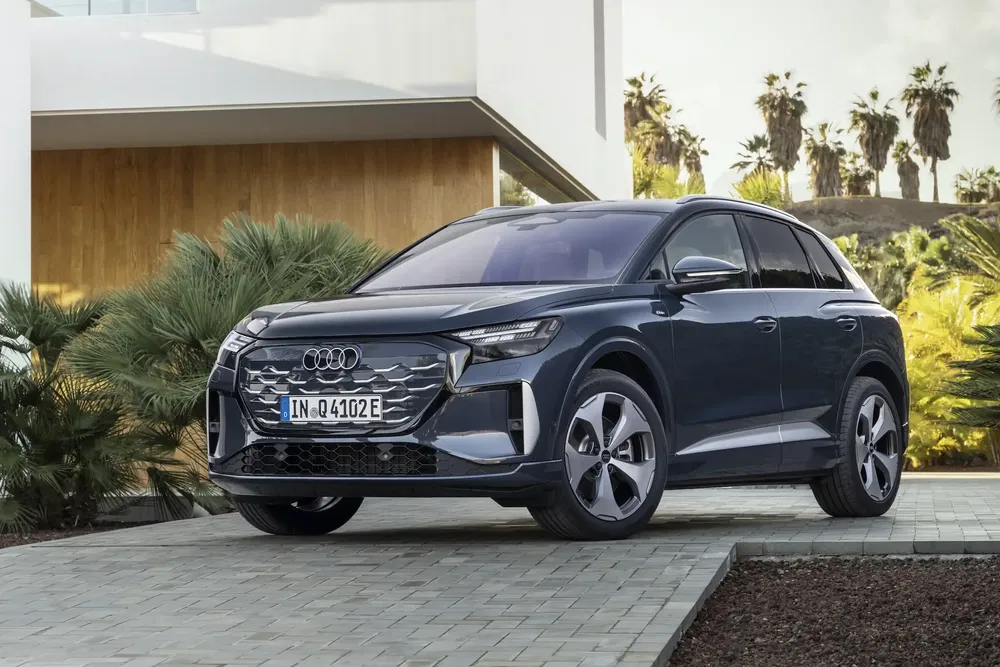 Audi Q4 e-tron garée devant une maison moderne, entourée de palmiers luxuriants.