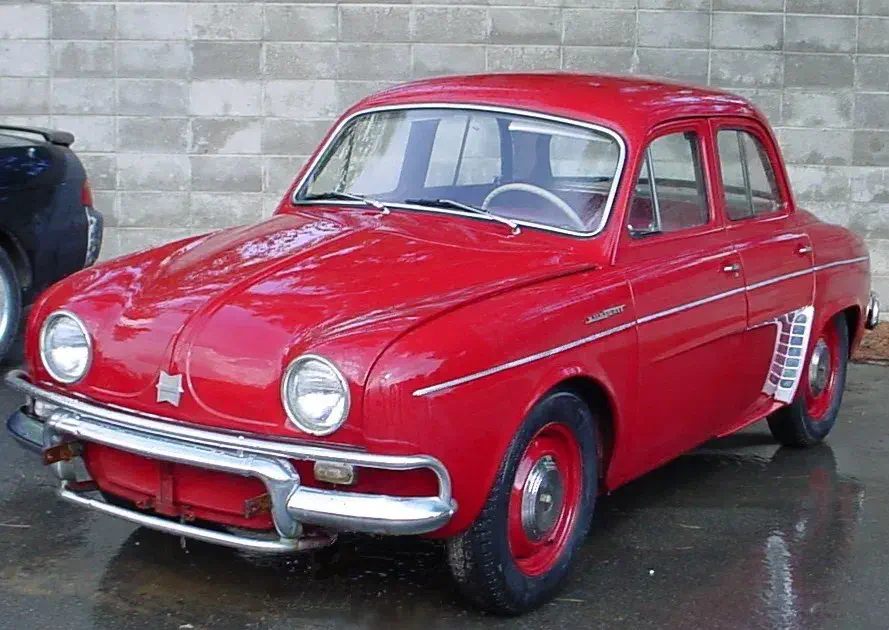 Renault Dauphine classique rouge garée devant un mur en briques grises.