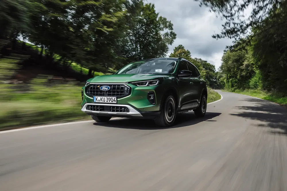 Ford Kuga vert roulant sur route sinueuse entourée d'arbres verdoyants.
