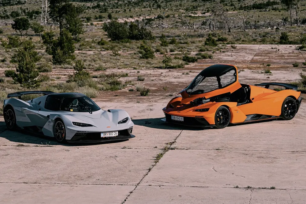 Deux voitures de sport KTM X-Bow sur une piste désertique, blanche et orange.
