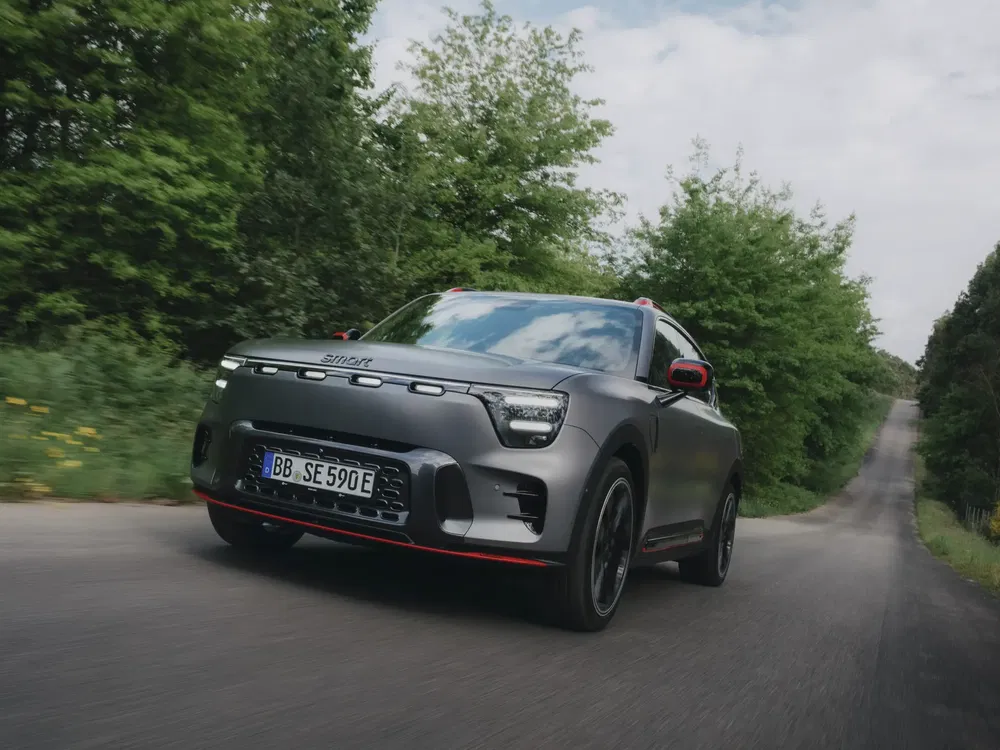 Elektrische Smart #1 rijdt op een door bomen omzoomde weg, dynamisch en modern ontwerp.