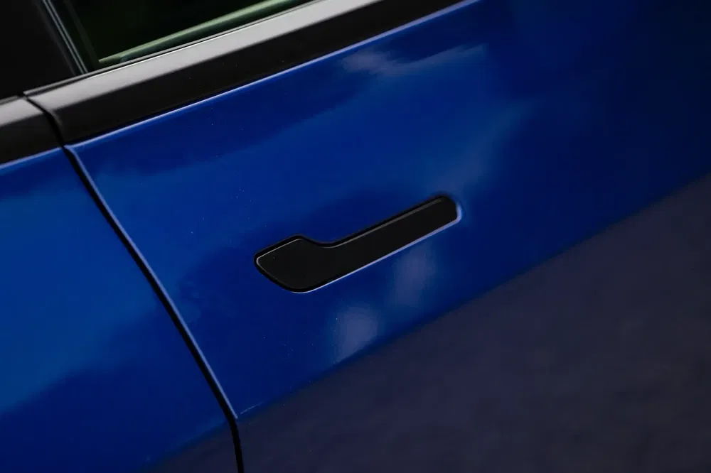 Gros plan de la poignée de porte encastrée d'une Tesla bleue, design moderne et épuré.