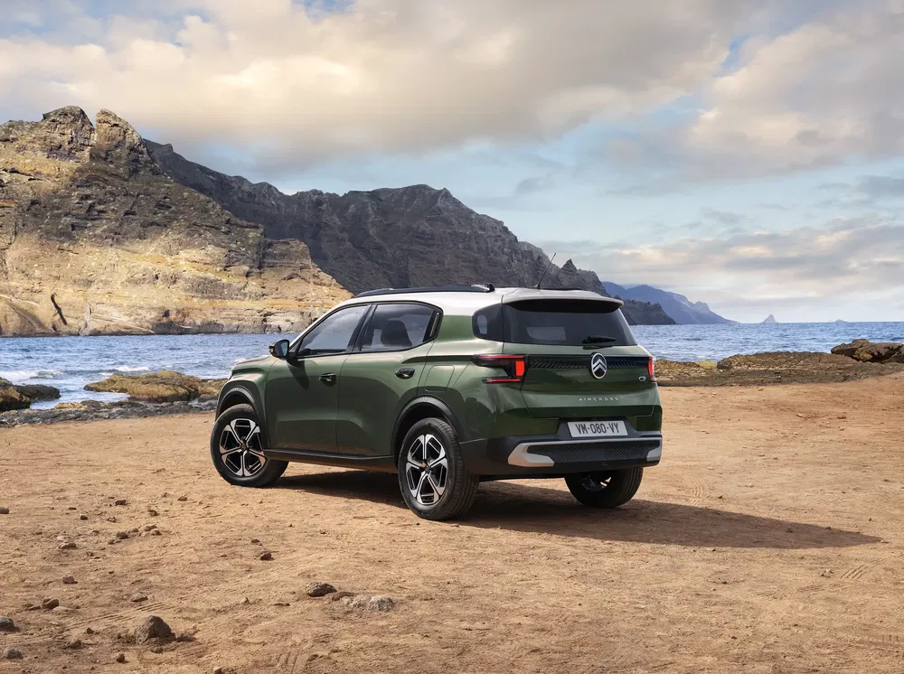 Groene Citroën C3 Aircross op rotsachtig strand met bergachtig en oceaan op de achtergrond.