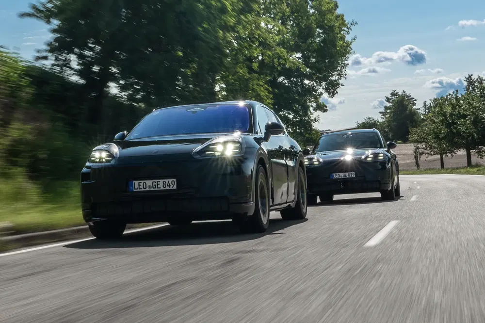 Deux Porsche électriques noires circulent sur une route bordée d'arbres par temps ensoleillé.