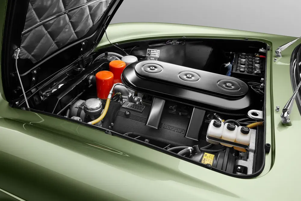Moteur Ferrari classique sous le capot d'une voiture verte, avec prise d'air noire distinctive.