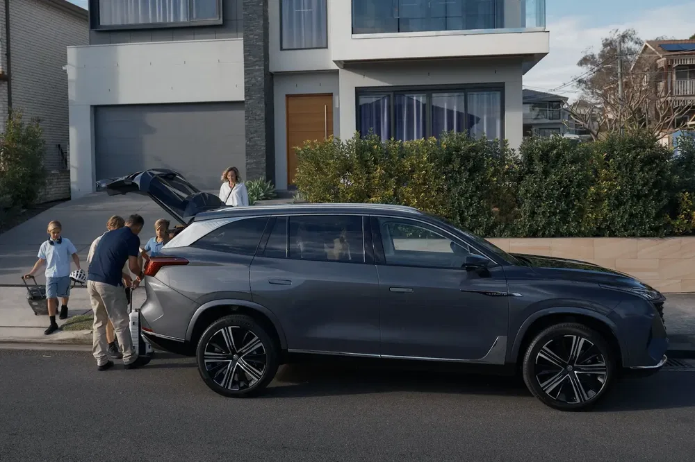 Elektrische gezinsauto geparkeerd voor een modern huis, bagage in de kofferbak.