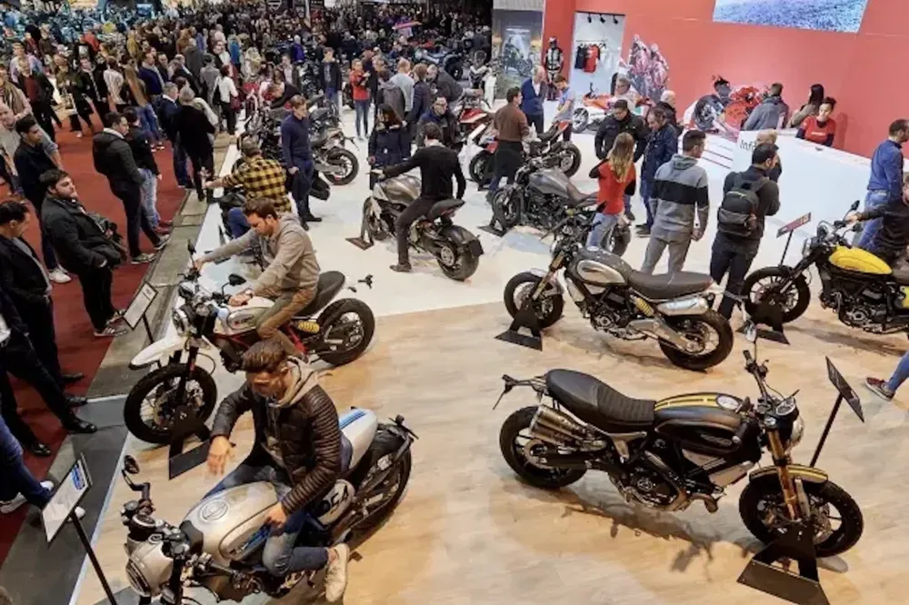 {"fr":"Salon de la moto bondé avec visiteurs essayant différents modèles Ducati, atmosphère animée.","nl":"Drukke motorshow met bezoekers die verschillende Ducati-modellen uitproberen, levendige sfeer."}